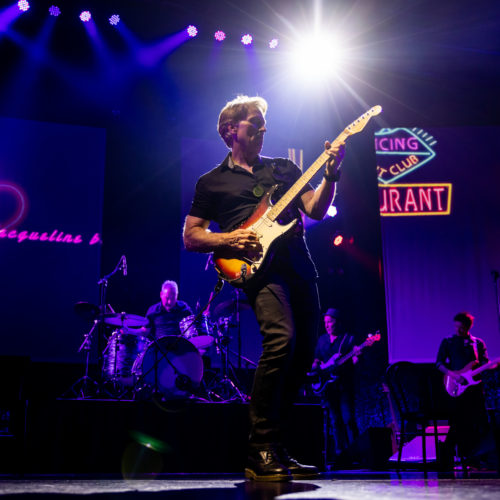 Electric guitarist performing under bright blue and purple stage lights