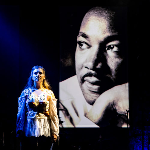 Female performer singing beside a large projected portrait of Martin Luther King Jr.