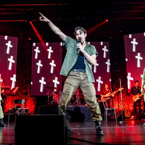 Male vocalist pointing above the stage as the band performs behind him